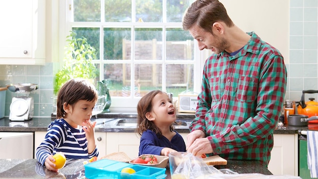 Un père prépare les boites à lunch de ses enfants.