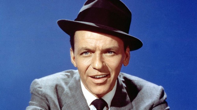 Frank Sinatra sur fond bleu, souriant, vêtu d'un chapeau melon et d'un élégant costume cravaté