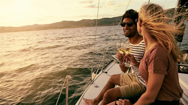 Un jeune couple prend un verre de vin sur un bateau de plaisance à la tombée du jour