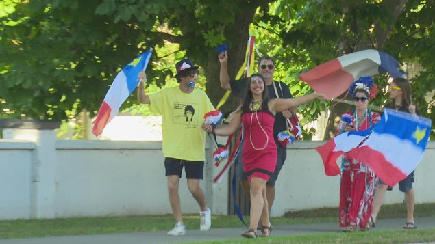 Des Acadiens sur le trottoir avec des drapeaux.