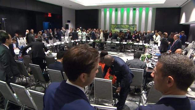 Une trentaine de personnes discutent et s'activent autour d'une grande table carrée où sont placées plusieurs rangées de chaises.