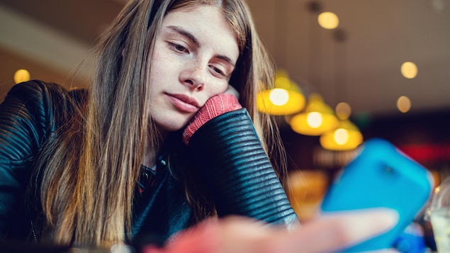 Une adolescente regarde son téléphone dans un café.