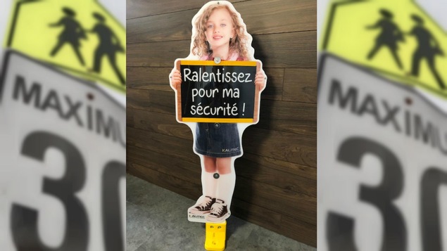 Une affiche d'une fillette tenant un tableau disant «Ralentissez pour ma sécurité».
