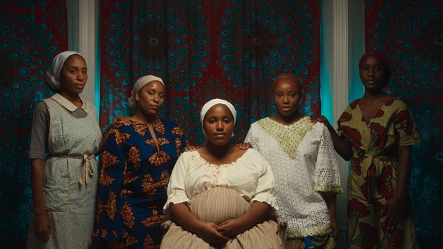 Cinq femmes à la peau noire regardent l'objectif. Celle de milieu est enceinte. 