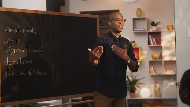 Le rappeur Webster (Aly Ndiaye) est devant un tableau dans une classe. 