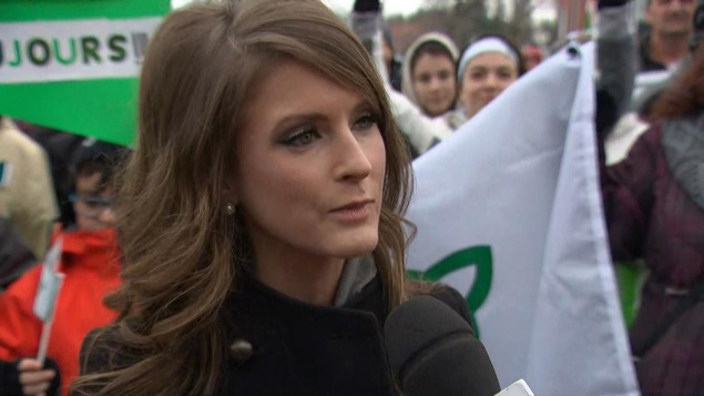 Amanda Simard répond aux questions d'une journaliste au milieu d'une foule.
