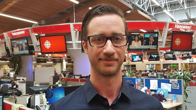 Un homme auxcheveuc bruns qui porte des lunettes et une chemise bleue.