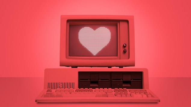 Une photo montrant un vieil ordinateur de bureau éclairé d'une lumière rouge dont l'écran affiche l'image d'un cœur.