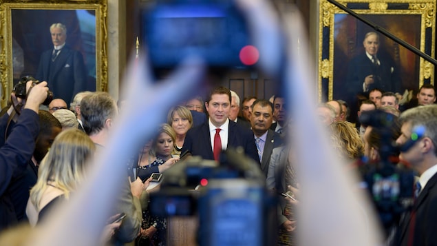 Les députés conservateurs sont serrés autour d'Andrew Scheer. À l'avant-plan, quelqu'un prend une photo de la scène.