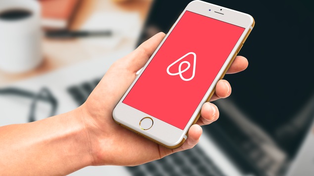 Une main tient un téléphone portable muni de l’application Airbnb.