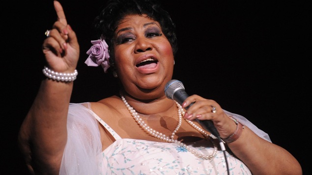 La chanteuse américaine Aretha Franklin tient un micro dans la main gauche et lève l'index de sa main droite.