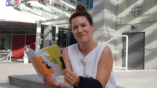 Assise devant l'entrée principale de Radio-Canada, elle tient le programme du théatre.
