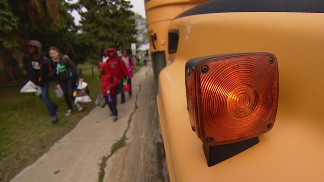 Gros plan sur une lumière d'un autobus scolaire. Des élèves floutés marchent à côté de l'autobus.