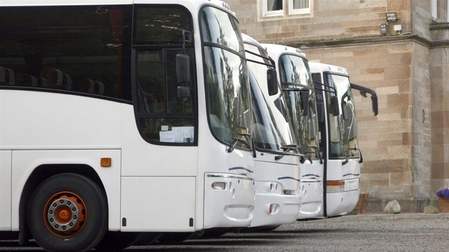 Quatre autocars blancs sont stationnés.