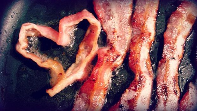 Du bacon qui cuit, dont une tranche est en forme de coeur.