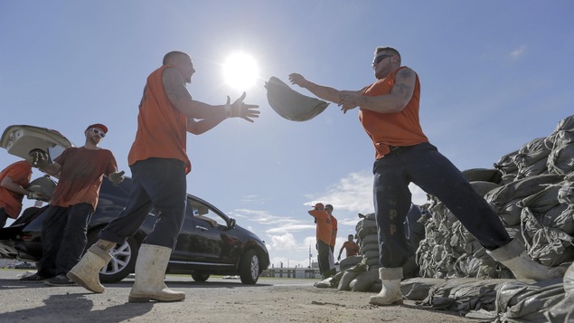 Des hommes chargent des sac de sable dans des voitures,