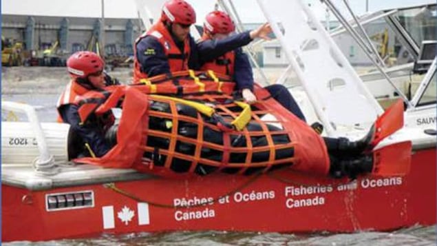 Des employés du ministère sur un petit bateau jettent à l'eau un radeau de sauvetage Des employés du ministère sur un petit bateau jettent à l'eau un radeau de sauvetage
