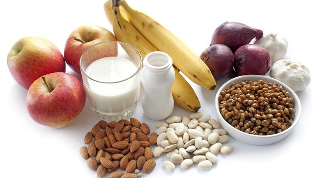 Des pommes, un verre de lait, des yogourts, des amandes, des oignons et de l'ail sur un fond blanc.