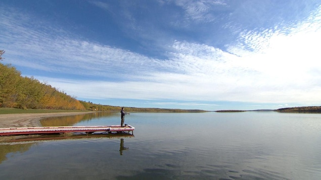 Un homme est sur un quai et pêche sur le Lac Beaver sous un ciel bleu.