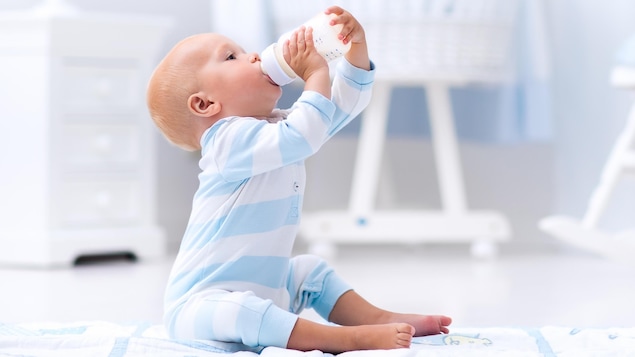 Un bambin boit goulûment à son biberon, vêtu d'un pyjama blanc et bleu Un bambin boit goulûment à son biberon, vêtu d'un pyjama blanc et bleu
