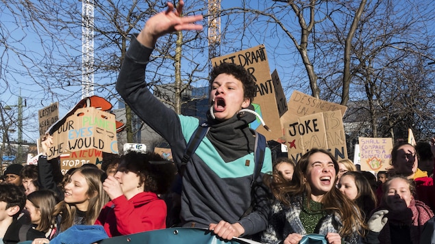 Un garçon crie avec la main levée entouré de ses amis brandissant des pancartes à la défense de la planète.