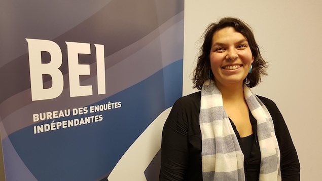 Mme Mollen Dupuis pose en souriant devant un panneau avec le logo du BEI.