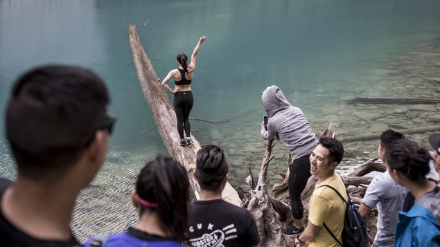 Une jeune femme fait une pose gracieuse sur un tronc à demi-submergé aux abords d'un lac du parc britanno-colombien de Joffre Lakes.