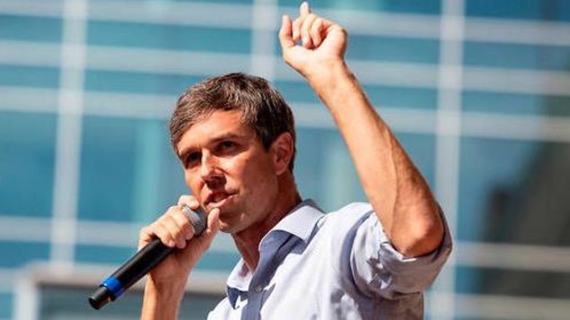 Beto O'Rourke tient un micro dans une main et lève l'autre main vers le ciel