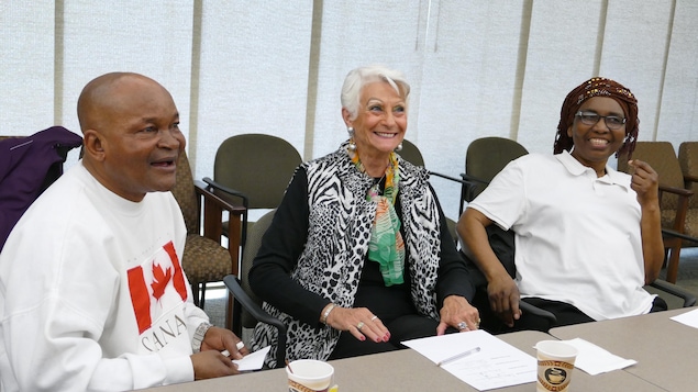 Un homme et deux femmes sont assis derrière une table et ils portent de grands sourires. Un homme et deux femmes sont assis derrière une table et ils portent de grands sourires.