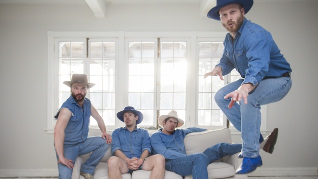 Photo des 3 membres du groupe sur un sofa et un autre qui saute.