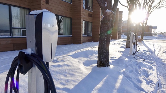 Une borne de recharge pour voiture électrique dans la neige en avant d'une résidence.