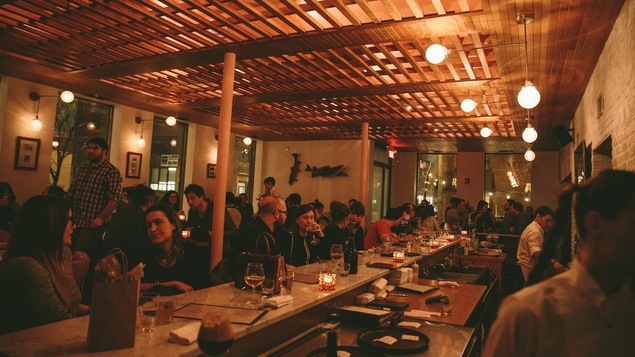Des gens sont assis à des tables et au comptoir à l'intérieur d,une brasserie avec des lumières tamisées.