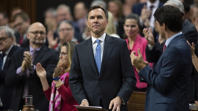 Le ministre parle debout; ses collègues applaudissent.
