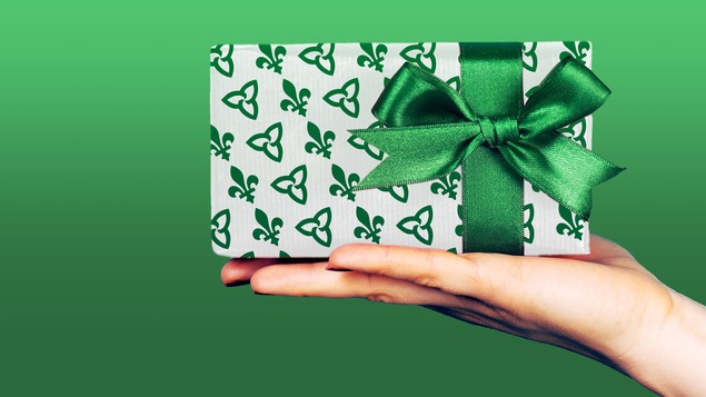 Une main présente un cadeau enveloppé dans un emballage aux couleurs du drapeau franco-ontarien. Une main présente un cadeau enveloppé dans un emballage aux couleurs du drapeau franco-ontarien.