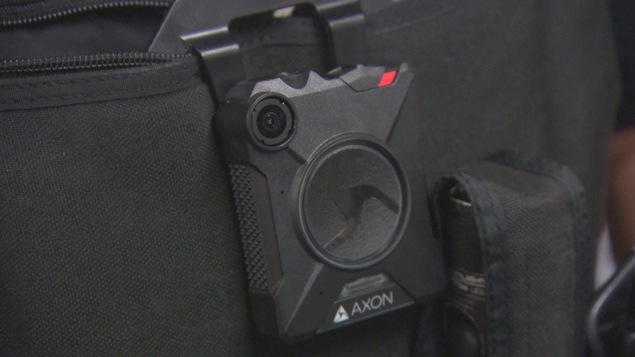 Zoom sur la caméra, plus petite qu'un téléphone cellulaire, sur le gilet d'un policier.