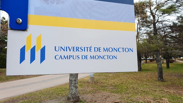 Le coin d'un panneau jaune et bleu sur lequel apparaît le logo de l'Université de Moncton et les mots « Université de Moncton Campus de Moncton ».