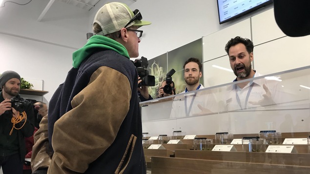 Un homme qui porte un blouson de sport parle à un autre homme au comptoir d'un magasin.