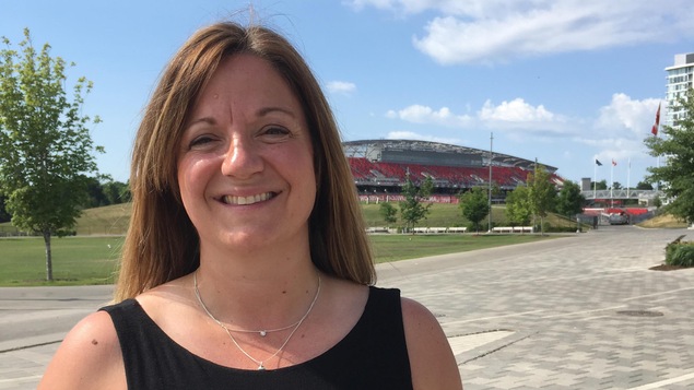 Une femme debout au soleil devant un stade de soccer à Ottawa.