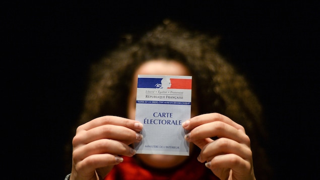Une femme montre sa carte électorale, en France. On peut y lire : « Liberté, égalité, fraternité. La République française ». Une femme montre sa carte électorale, en France. On peut y lire : « Liberté, égalité, fraternité. La République française ».
