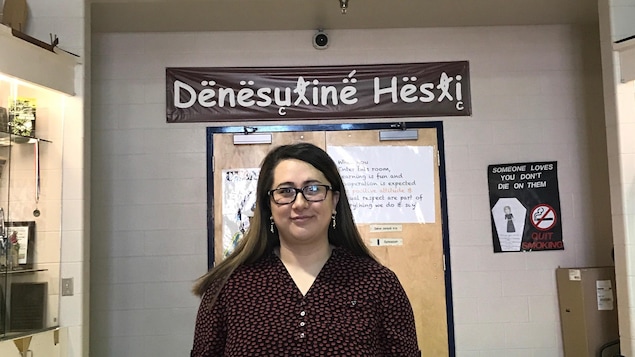 Une femme souriante dans un couloir, sous une bannière avec une inscription en dene.