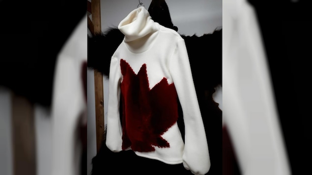 Une chandail à col roulé en laine polaire arbore une feuille d'érable rouge en fourrure.