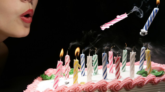 Une dame souffle fort sur les bougies d'un gâteau d'anniversaire et deux d'entre elles volent dans les airs.