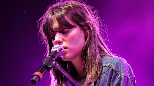 La chanteuse Charlotte Cardin chante les yeux fermés avec un micro très près de sa bouche. La chanteuse Charlotte Cardin chante les yeux fermés avec un micro très près de sa bouche.