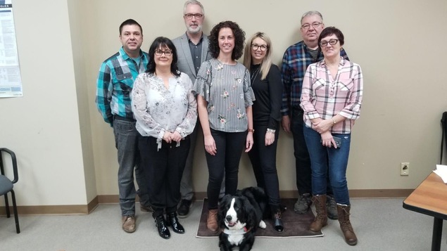 Trois hommes et quatre femmes posent en compagnie d'un chien d'assistance.
