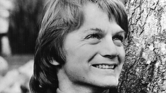 Le chanteur français Claude François, appuyé sur un tronc d'arbre, regarde le ciel.