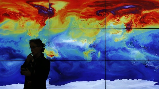 Une femme devant une carte numérique du monde qui montre les variations de températures.