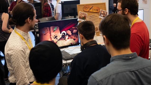 Une photo montrant un groupe de personnes en train de regarder un écran d'ordinateur pendant que l'un d'entre eux joue à un jeu vidéo.