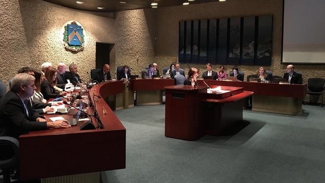 Les conseillers et le maire de Trois-Rivières, assis autour de la table de la salle du conseil, font face au public qu'on ne voit pas. La greffière de la Ville assise devant eux, faisant aussi face au public dans la salle.