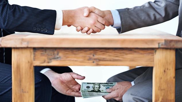 Mise en scène montrant deux hommes se serrant la main au-dessus de la table et échangeant une liasse de billets de banque en dessous de la table.