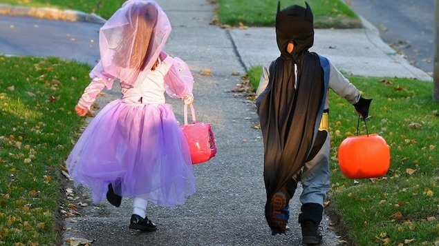 Deux enfants courent dans la rue avec des sacs pour ramasser des friandises. Ils sont déguisés pour l'Halloween.